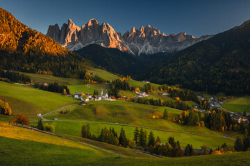 Fototapeta na wymiar Autumn sunset in Val di Funes in the Italian Dolomites. Fall colors create beautiful contrasts with the blue sky.
