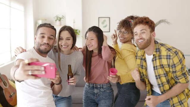 Multiethnic young friends celebrating at home party - Diverse group of millennial people having fun dancing and drinking together while taking selfie photo