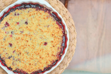 round berry pie in baking dish on placemat. crumble blueberry cobbler. home baking, healthy meal,...