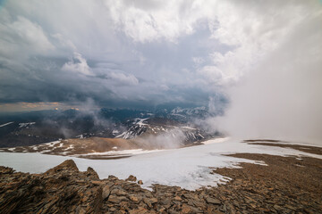 Awesome top view through clouds to high snowy mountains. Scenic landscape with beautiful snow mountains in low clouds. Atmospheric alpine view from stone hill to snow mountain range with low clouds.