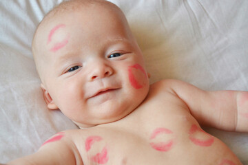 The image of a charming child with red kisses on the skin, a happy boy isolated on a white background, a little angel of love, a romantic holiday, the concept of Valentine's day