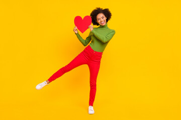Full body photo of young cheerful girl good mood hold paper heart cupid romantic isolated over yellow color background