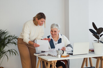 two women working together at workplace with desk and laptop