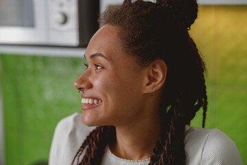 Close up of cheerful young mixed-race woman with smile on face looking away in room
