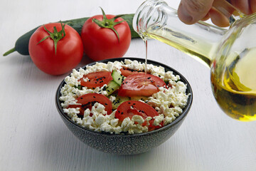 Pouring olive oil salad of fresh tomatoes, cucumbers, cottage cheese and black cumin