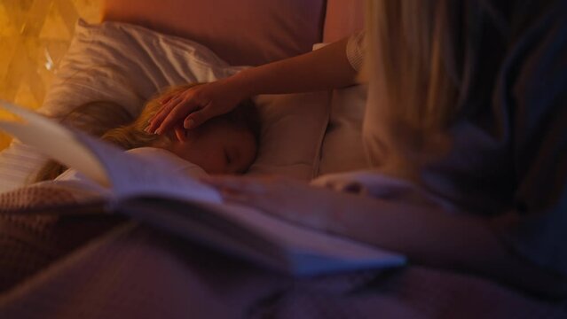 Mother with book takes care of daughter sleeping on bed
