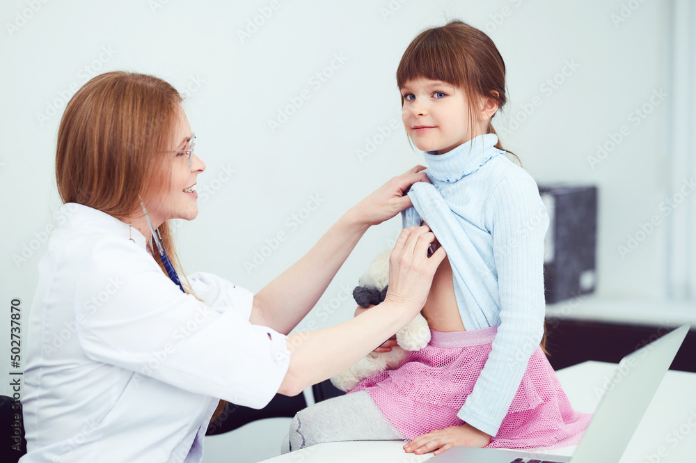 Wall mural caucasian female doctor examining patient little girl by stethoscope in office