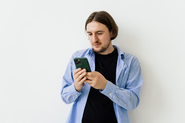 Young smiling businessman watching something on mobile phone isolated on white background. Studio shoot. Copy space