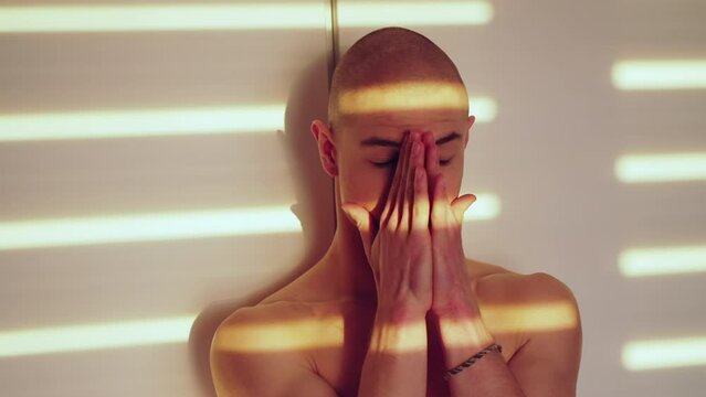 Sad upset caucasian bald gay man standing and covering his face with both hands. Beautiful sunshine on the walls and his body. High quality 4k footage