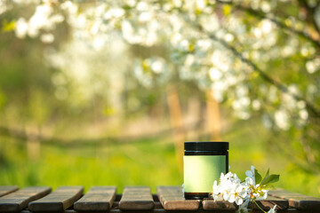 Cosmetic jar on wooden table in blooming tree spring garden