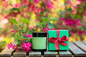 Cosmetic bottle and gift box on wooden table in spring time blooming garden