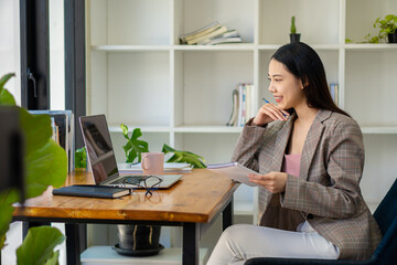 Obraz premium Successful Asian businesswoman uses computer and internet to work from home. Cute girl creating freelance typing on laptop for online chatting, teleconferencing with customers.