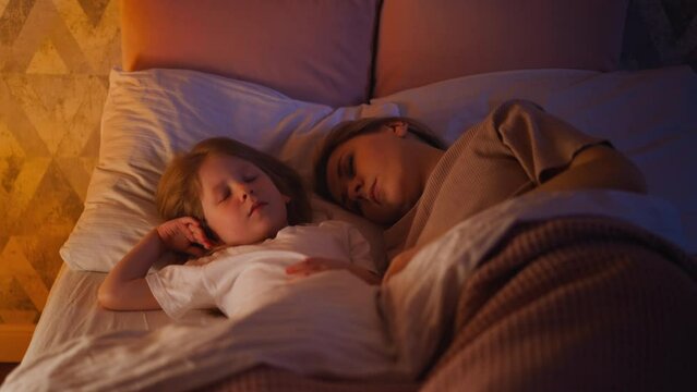 Pretty little girl and mommy sleep in wide bed at night