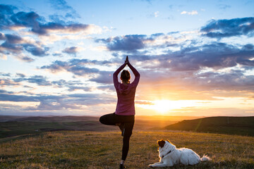 woman with white dog doing yoga at sunset tree pose  vrksasana