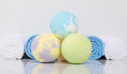 close-up of multicolored bath salts, in the form of bombs and towels wrapped in a roll, on a white table with a reflection