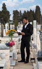 Prayer in a jewish cemetery in Israel. Judaic Tombstones with shallow depth of field. Selective focus. Old jewish cemetery in the forest. Bearded Jew in black kippah reads a Hebrew Bible, praying.