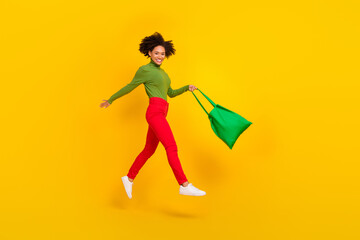 Full body profile side photo of young cheerful girl have fun jump hold shopper bag market isolated over yellow color background
