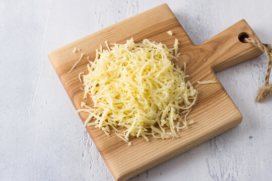 Wooden board with grated cheese on gray background, flat lay, close-up