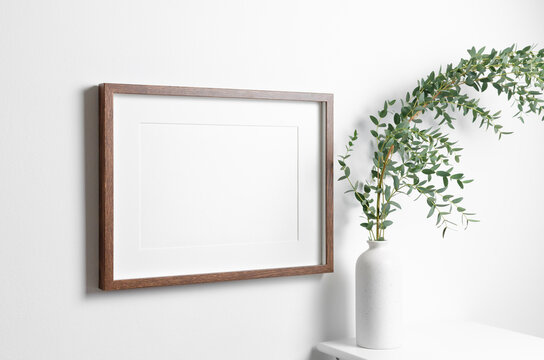 Blank frame mockup for artwork or picture on white wall with eucalyptus twigs.