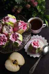 Blurred image of a marshmallow in the form of flowers, a cup of coffee, an apple and flowers on a black background. Still life.