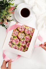 Blurred image of a cup of coffee, flowers and a girl's hand opening a box with a sweet gift.