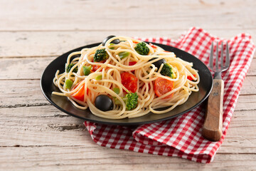 Spaghetti with vegetables(broccoli,tomatoes,peppers) on wooden table