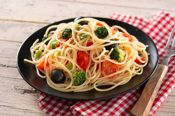 Spaghetti with vegetables(broccoli,tomatoes,peppers) on wooden table