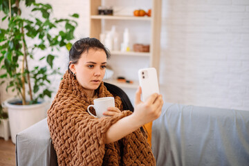 Close-up of a woman holding a mug of tea in her hand, and talking on a video call with her doctor. A woman who feels unwell calls a doctor over the Internet.