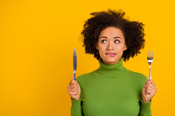 Portrait of attractive cheery sly minded wavy-haired girl holding knife copy space isolated over bright yellow color background