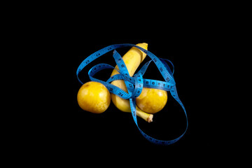 A yellow ripe banana and two plums, covered with a blue measure tape. Symbolic shot: measuring...