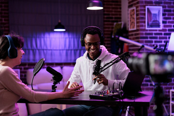 Cheerful people meeting in studio to film podcast episode on camera, recording live broadcast conversation to create internet content. Man and woman chatting on streaming web show.