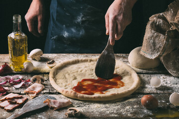 chef spreads tomato sauce on a pizza base while preparing 