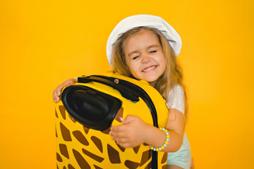 portrait of a cute smiling girl in a white hat with a suitcase, studio photo on a yellow background, vacation concept