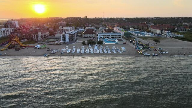 Drone flying from the sea towards the coast with the hotel beach at sunset