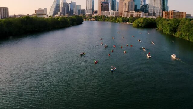 Kayakers on Town Lake in Austin, Texas paddle towards the downtown skyline at golden hour during sunset 4k aerial drone tilt up