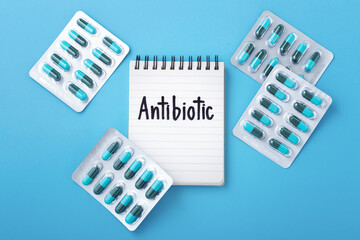 Antibiotic word on notebook with capsule pills in pack on blue background