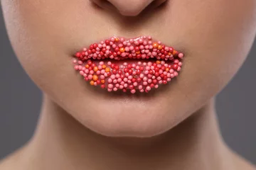 Junge Frau mit schönen Lippen bedeckte Süßwarenstreusel auf grauem Hintergrund, Nahaufnahme © New Africa
