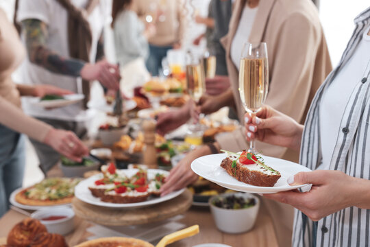 Woman with glass of champagne and sandwich near brunch buffet indoors, closeup. Space for text