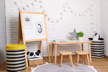 Stylish child room interior with wooden table and board near white brick wall