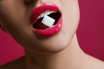 Woman with beautiful lips eating sugar cube on pink background, closeup