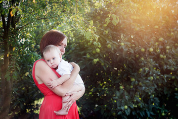 Mama przytula maluszka w objęciach, pod drzewem w promieniach letniego słońca