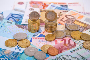 A stack of ruble coins and euro coins on the background of paper money, close-up