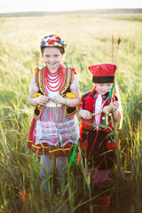 Dzieci w tradycyjnych polskich krakowskich strojach spacerują po polu obsianym zbożem w ciepłych letnich promieniach słonca - obrazy, fototapety, plakaty