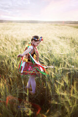 Dziewczynka ubrana w tradycyjny polski strój krakowianki sypie kwiatki i tańczy w zbożu - obrazy, fototapety, plakaty