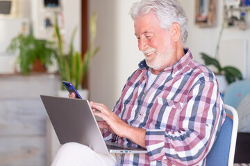 Elderly bearded man sitting at home holding mobile phone. Joyful and smiling beautiful senior man enjoying tech and social