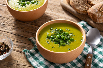 Green pea soup in a wooden bowl on rustic wooden table	