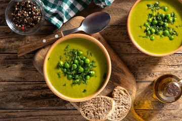 Green pea soup in a wooden bowl on rustic wooden table. Top view
