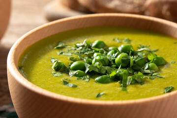 Green pea soup in a wooden bowl on rustic wooden table. Close up