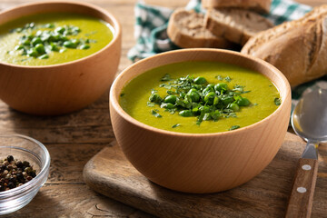Green pea soup in a wooden bowl on rustic wooden table	