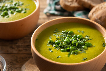 Green pea soup in a wooden bowl on rustic wooden table	